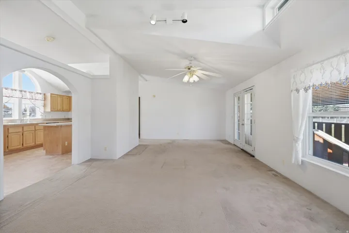 Spacious interior room with light-colored carpeting, white walls, and a vaulted ceiling