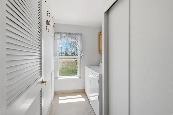 Dedicated laundry area featuring a single window, overhead cabinetry, and light-colored carpeting