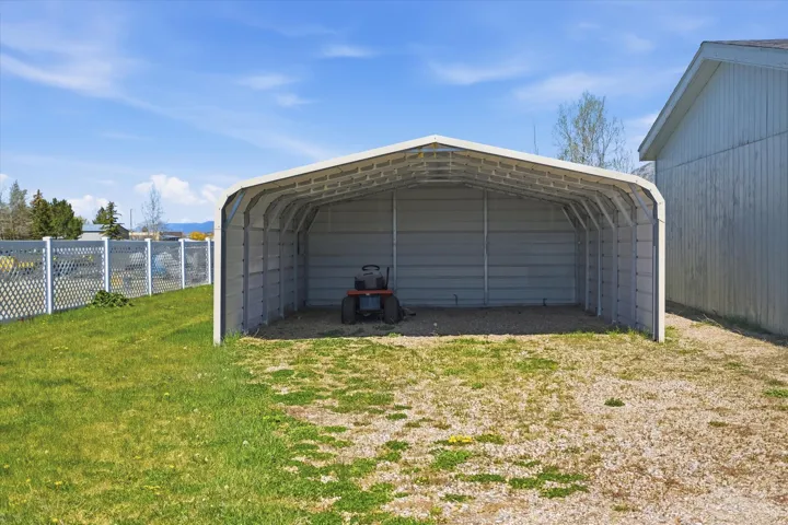Metal carport with a gravel base, bordered by a green lawn and white lattice fencing
