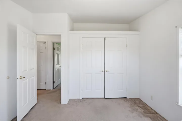Interior room featuring neutral-toned carpet flooring, white painted walls, and a white six-panel interior door with brass hardware