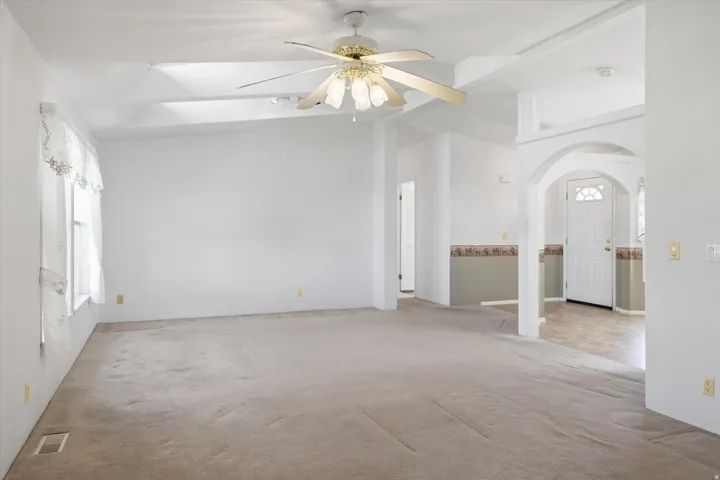 Spacious interior room featuring vaulted ceilings, a ceiling fan with integrated lighting, and carpeted flooring