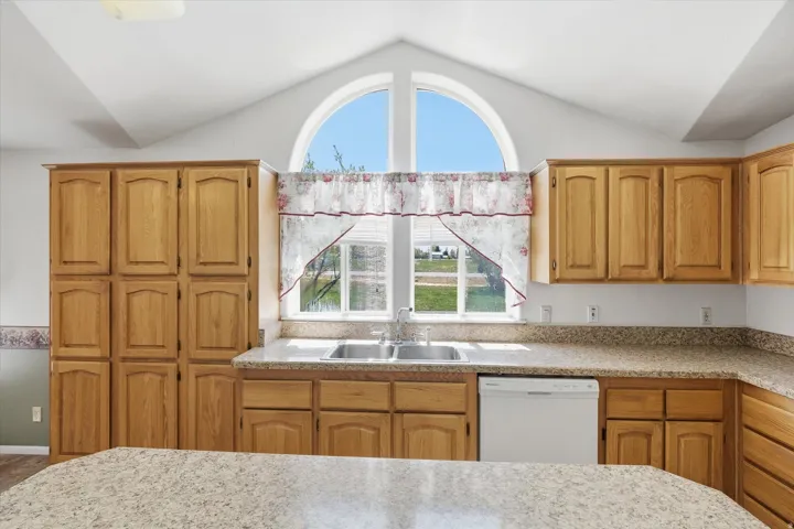 Kitchen featuring light wood cabinetry, a double basin stainless steel sink, and light speckled countertops