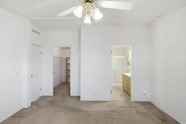 Carpeted room featuring a ceiling fan with light fixture, a closet with built-in shelving, and an en-suite bathroom entrance with a wood-finish vanity and glass-enclosed shower