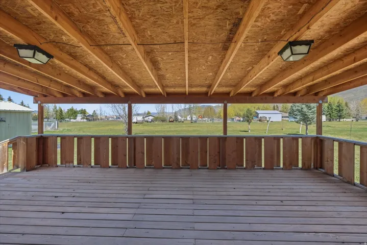Spacious covered deck featuring wood decking, exposed wood beam ceiling, and two ceiling-mounted light fixtures