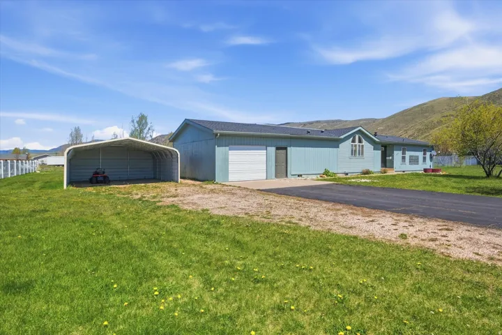 Expansive green lawn with a paved driveway and gravel parking area