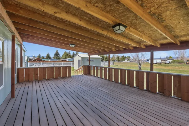 Expansive wood-finish deck with a built-in wood railing, supported by exposed wood beams, and illuminated by two ceiling-mounted fixtures