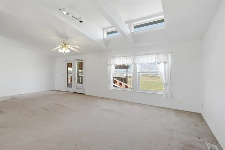 Spacious room featuring vaulted ceilings with exposed beams, track lighting, and a ceiling fan
