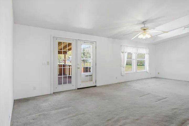 Spacious room featuring light-colored carpeting, white walls, and a white ceiling fan with integrated lighting