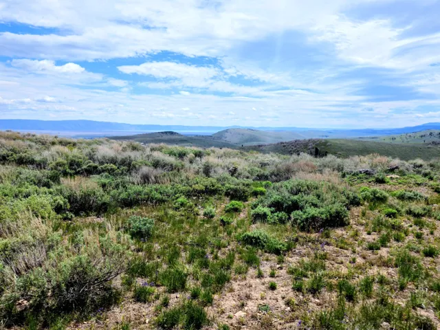 Expansive natural landscape featuring rolling hills and distant mountains under a blue sky with scattered clouds