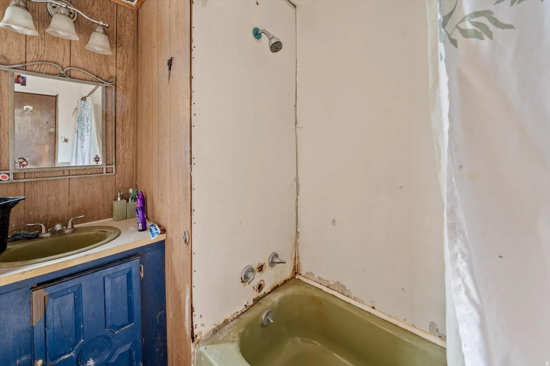 Bathroom featuring a green bathtub, shower fixture, and a vanity with a green sink and blue cabinetry