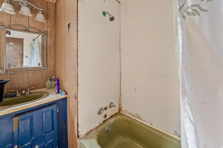Bathroom featuring a green bathtub, shower fixture, and a vanity with a green sink and blue cabinetry