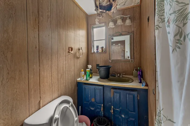 Bathroom featuring wood-finish paneling, a single window, vanity with painted blue cabinetry, and a white toilet