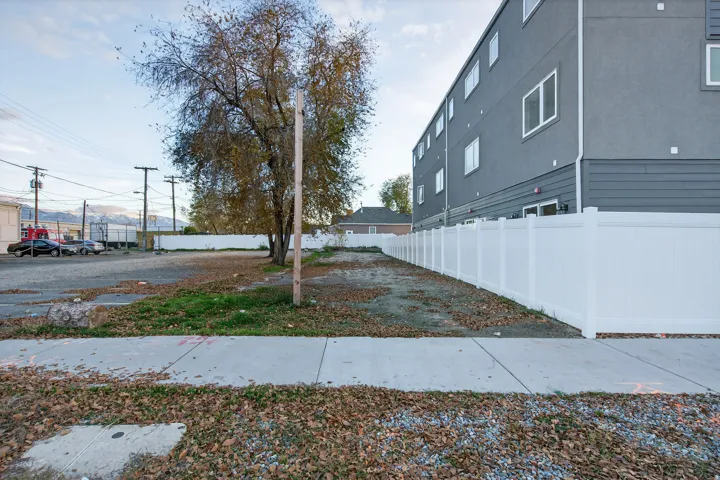 Cleared lot with established tree, adjacent to a contemporary multi-story building featuring a gray stucco and siding exterior