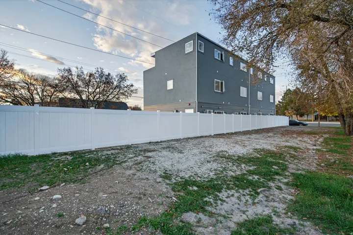 Expansive lot featuring a white privacy fence bordering a multi-story building with a gray exterior finish and multiple window placements