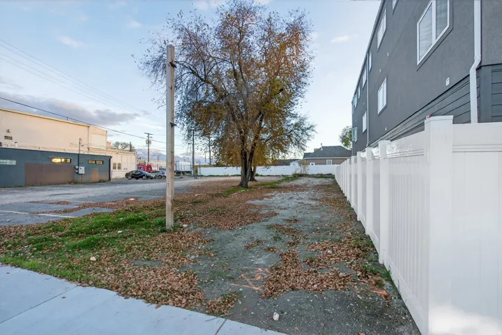 Cleared lot featuring a mature tree, a white panel fence, and a concrete sidewalk border