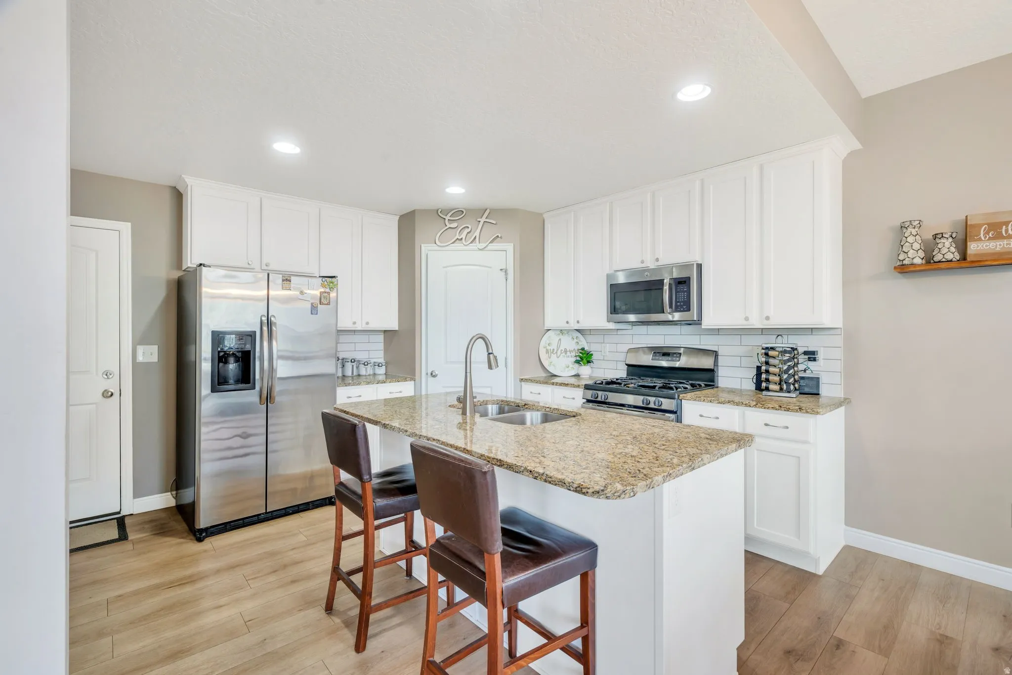 Kitchen featuring a central island with a stone countertop and seating, stainless steel appliances, white cabinetry, a subway tile backsplash, and wood-finish flooring