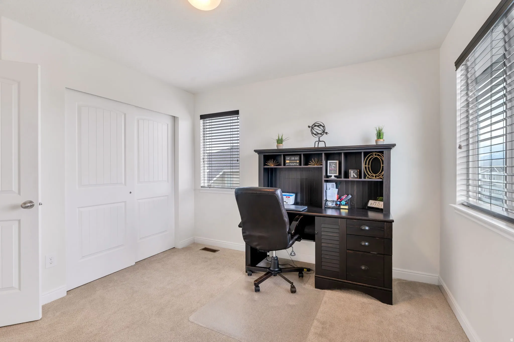 Neutral carpet flooring paired with white walls, featuring a window with horizontal blinds and a double-door closet with panel detailing