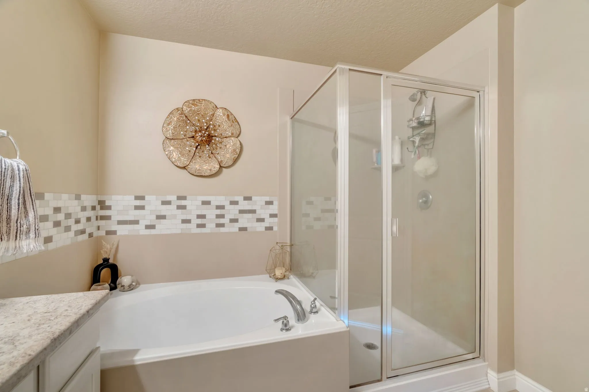 Full bath featuring a built-in soaking tub, a separate glass-enclosed shower, a tiled accent wall, and a vanity with a light-toned countertop