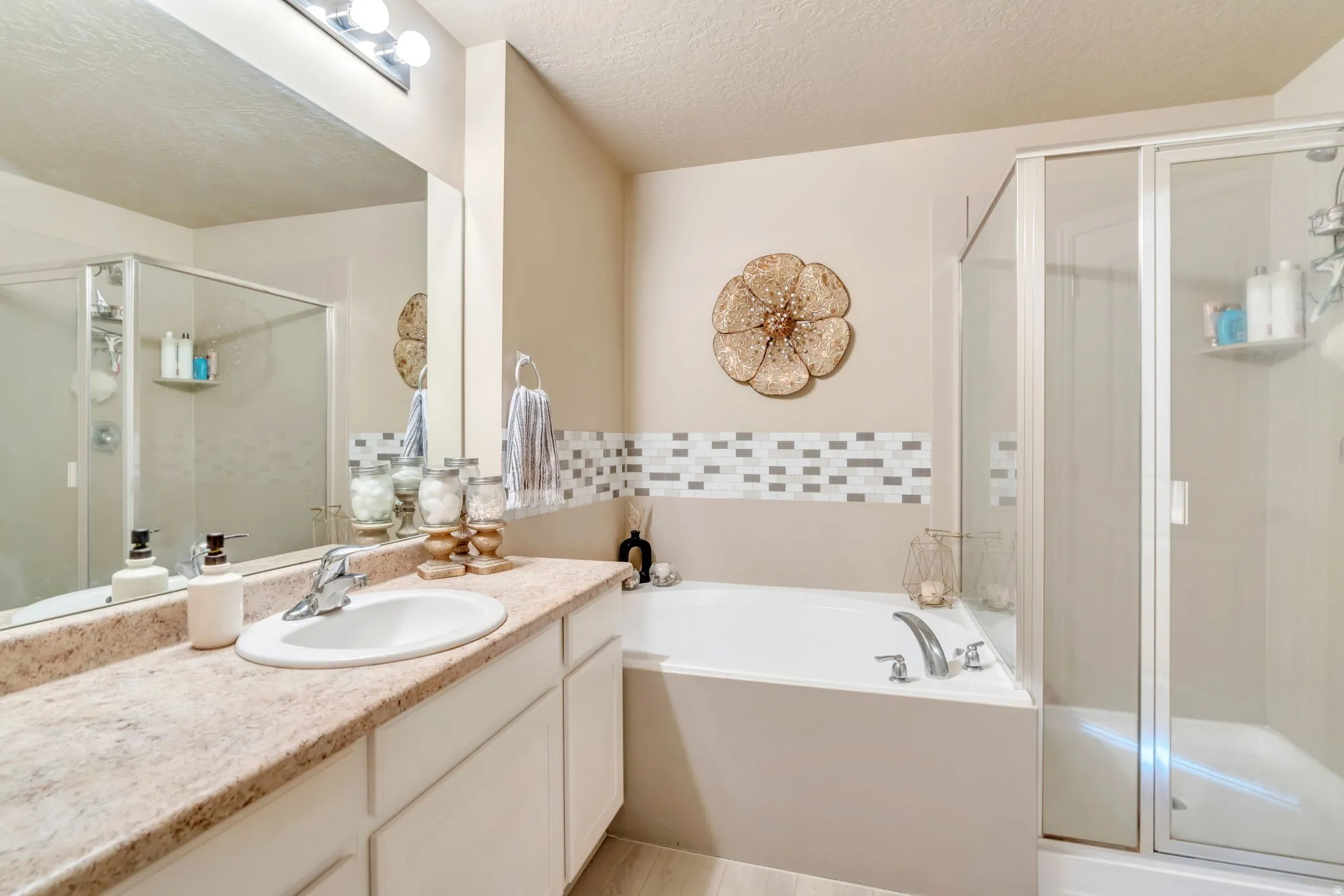 Bathroom featuring a single vanity with an oval sink, a built-in soaking tub, and a separate glass-enclosed shower