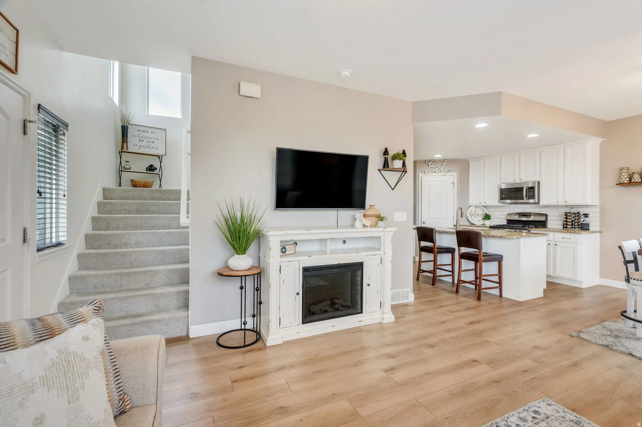 Open-concept living space featuring wood-finish flooring, a contemporary fireplace, and a staircase with light gray carpeting