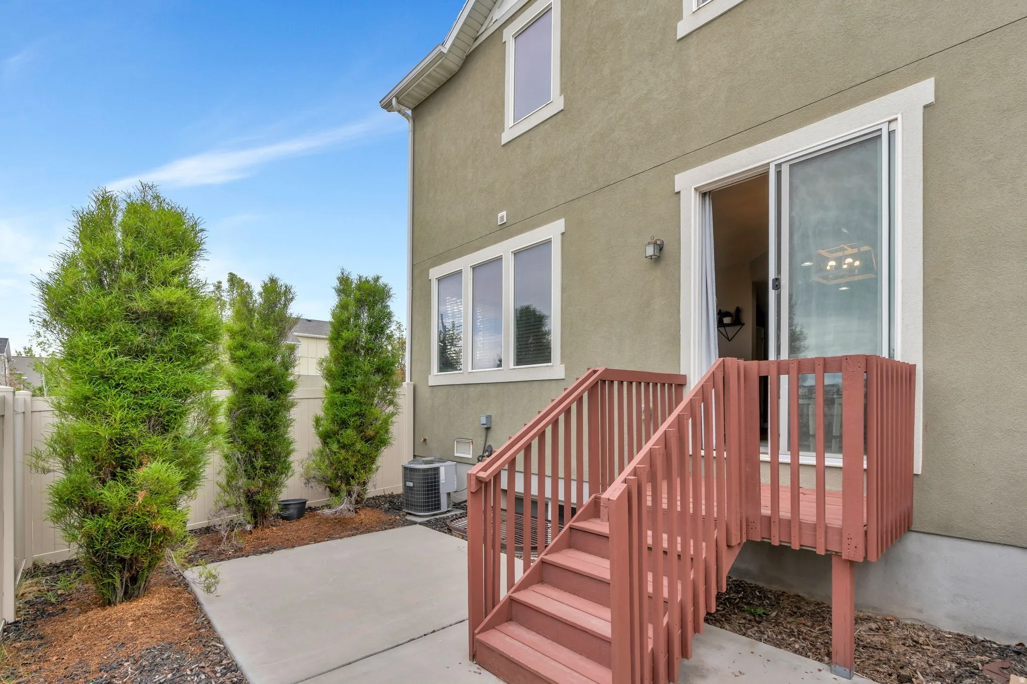 Private patio featuring a red-stained wood deck with stairs, a sliding glass door, and stucco exterior