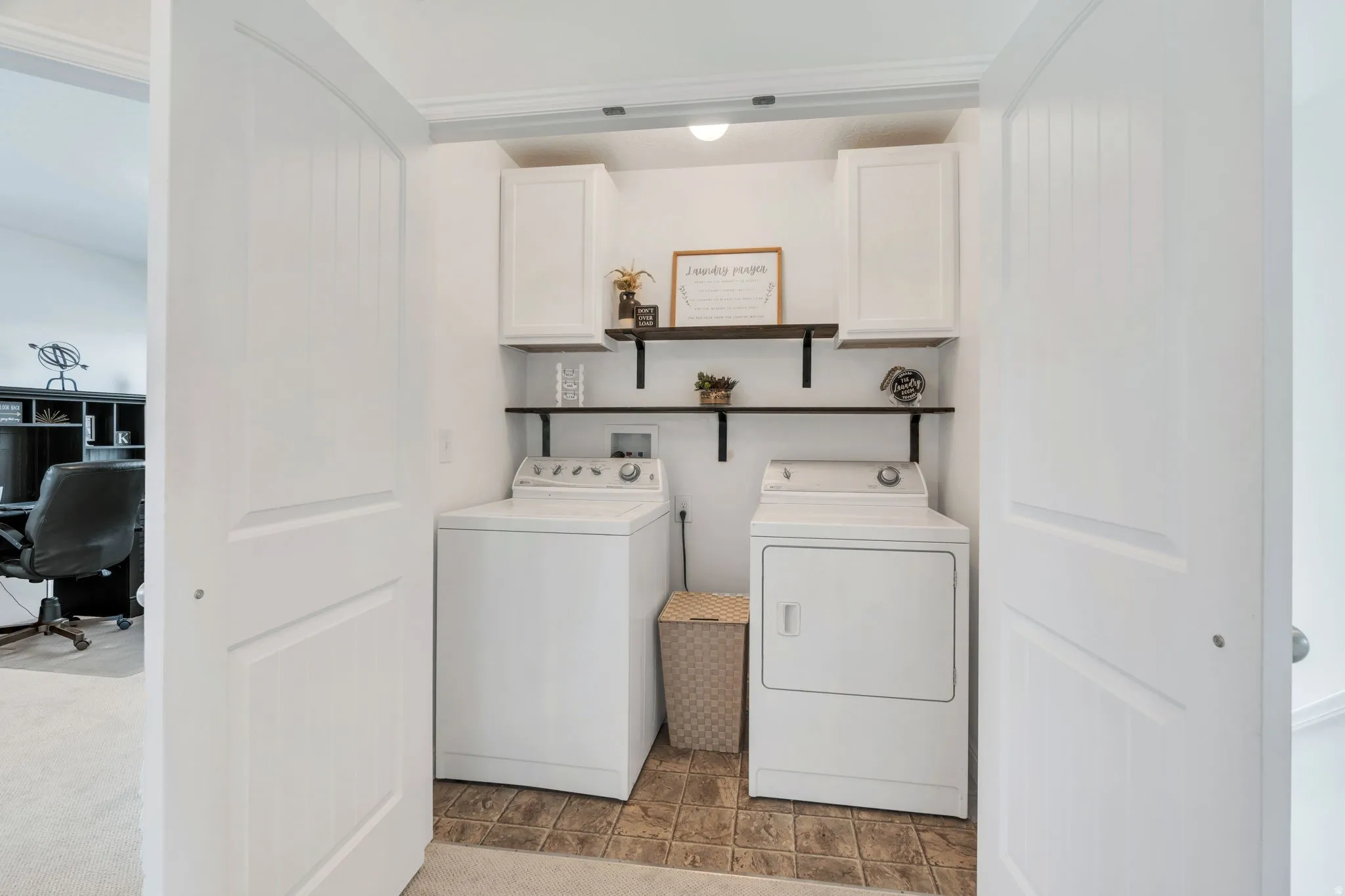 Functional laundry area featuring white cabinetry, open shelving with black brackets, and a light-toned tile floor