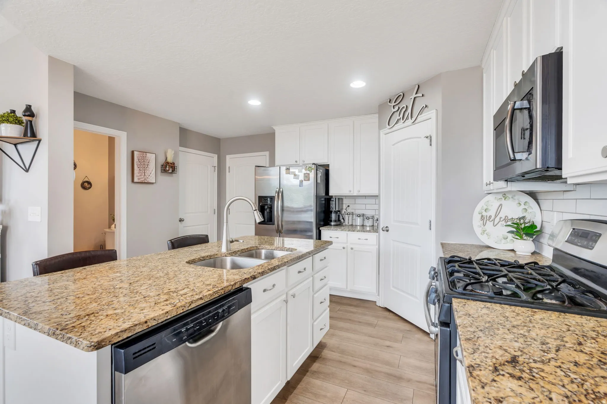 Kitchen featuring an island with double sinks, stainless steel appliances, white cabinetry, and wood-finish flooring