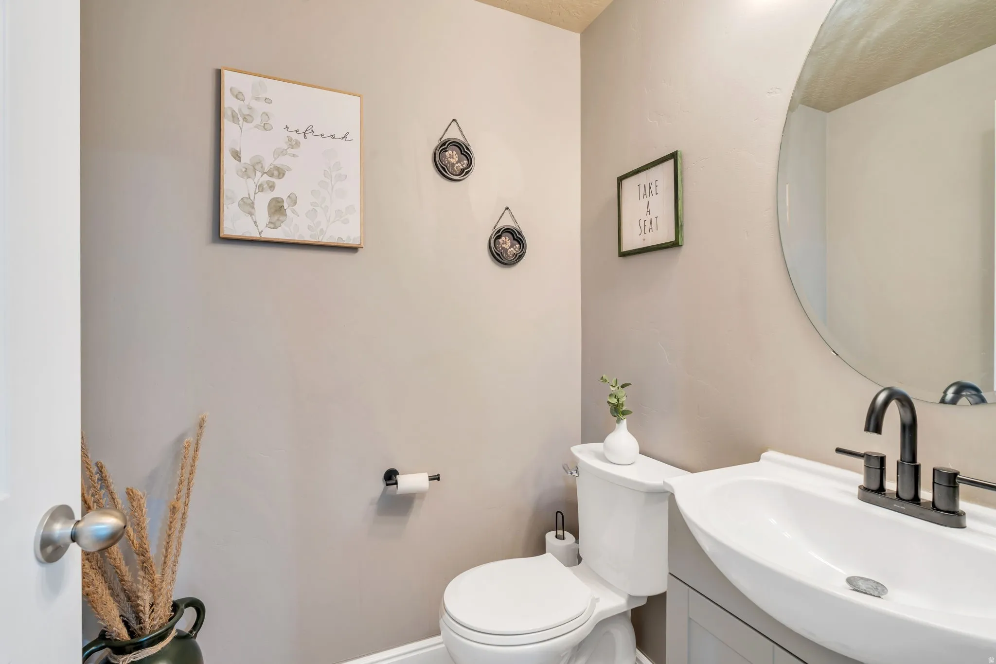 Pedestal sink with matte black faucet, wall-mounted mirror, and neutral wall paint