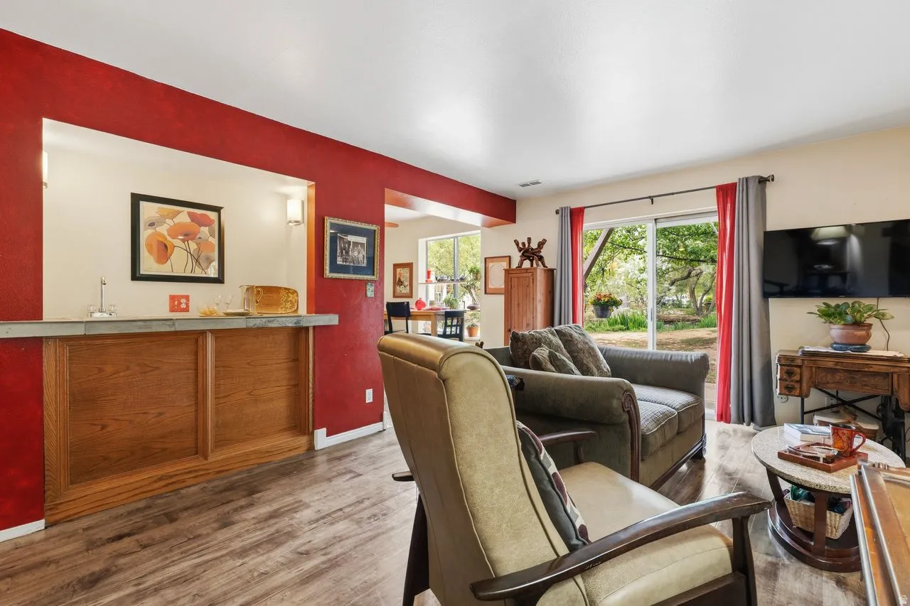 Spacious living area featuring wood-finish flooring, a built-in wet bar with a countertop and under-cabinet storage, and bright accent walls