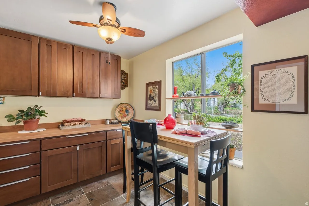 Dinning/Kitchen featuring a large window, wood-finish cabinetry, butcher block-countertops, ceiling fan with integrated lighting, and slate tile flooring