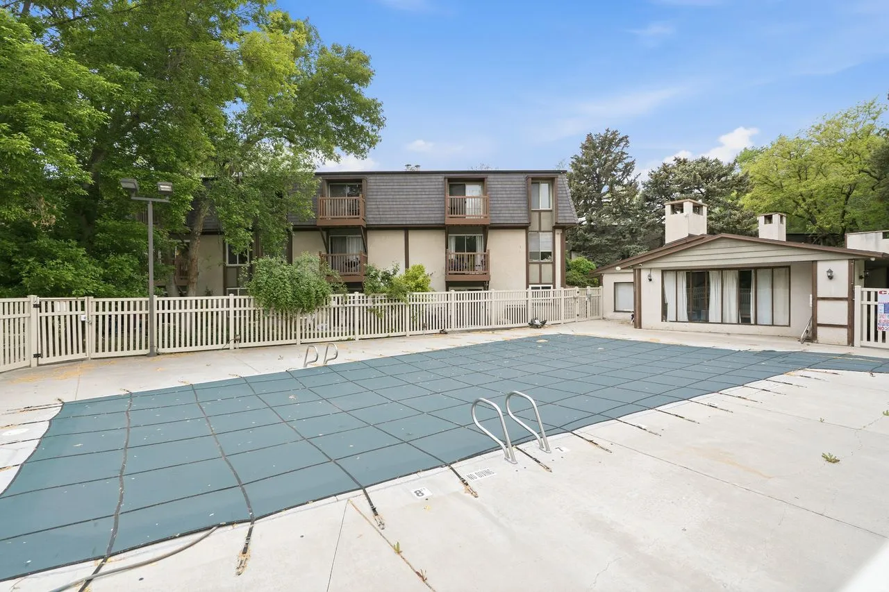 Outdoor swimming pool area with concrete surround, white picket fencing, and adjacent building with multiple balconies