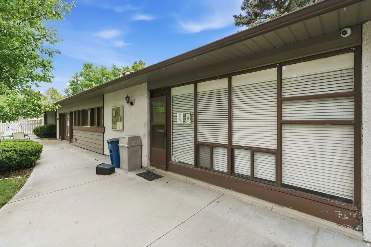 Exterior entrance featuring a concrete walkway, multiple windows with horizontal blinds, and a brown framed door