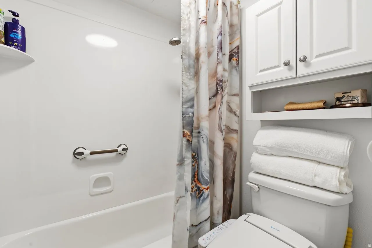 White acrylic tub and shower combination featuring a grab bar and integrated soap dish