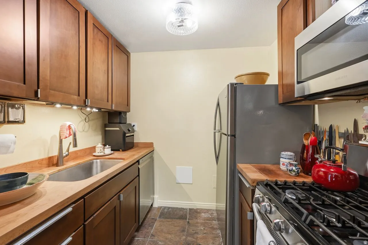 Kitchen featuring newer wood-finish cabinetry, butcher countertops-newer like appliances with Gas Range-Microwave-Refrigerator & plenty of countertop space with under mount lighting & plenty of storage.