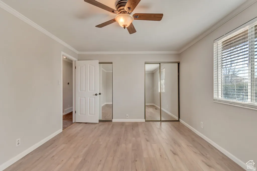 Unfurnished bedroom with two closets, light wood finished floors, a ceiling fan, and ornamental molding
