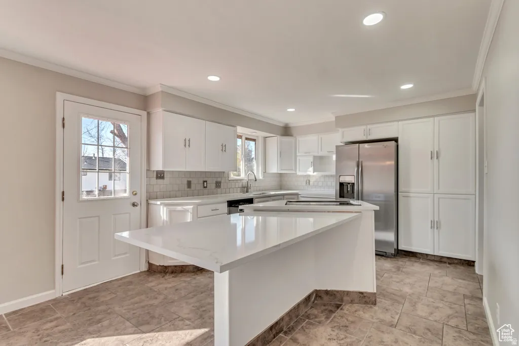 Kitchen with white cabinets, stainless steel appliances, a center island, crown molding, and tasteful backsplash