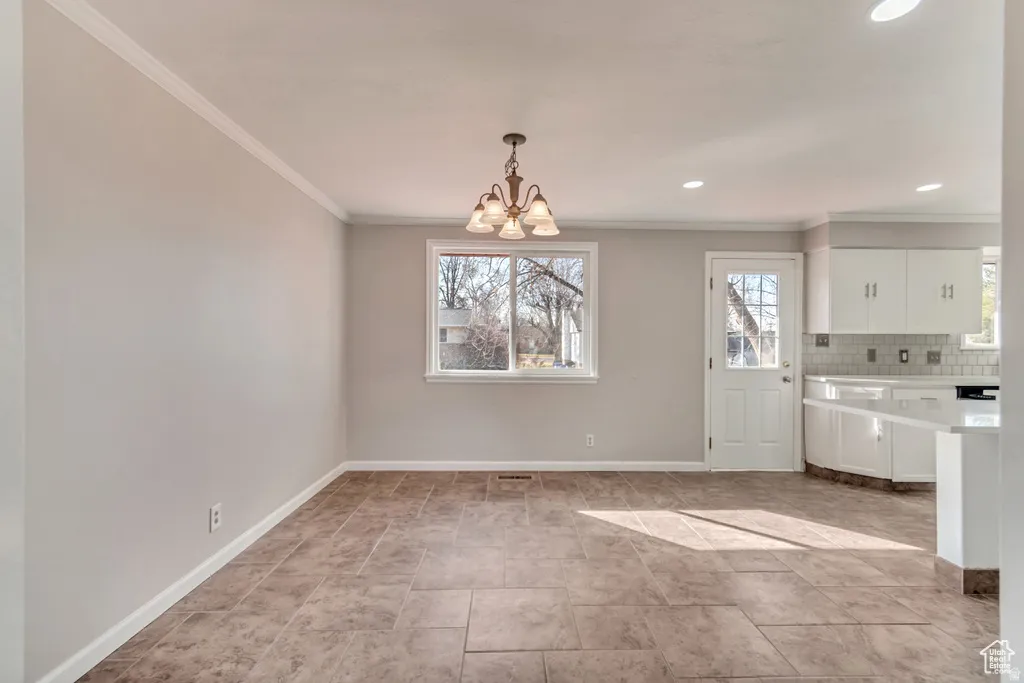 Unfurnished dining area with a chandelier, crown molding, and healthy amount of natural light