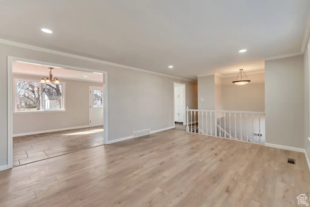 Spare room with light wood-style floors, ornamental molding, and suspended lighting
