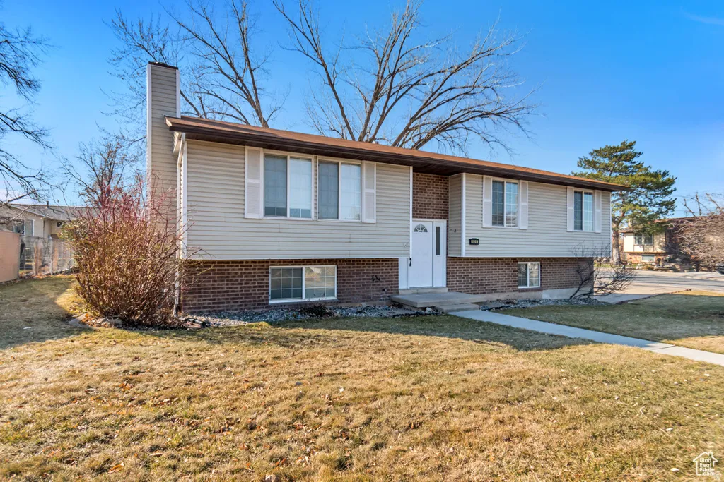 Raised ranch with a chimney, a front lawn, and brick siding