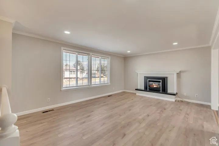 Unfurnished living room featuring crown molding, a lit fireplace, light wood-type flooring, and recessed lighting