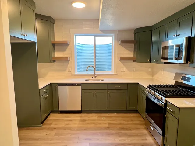 Kitchen featuring olive cabinetry, light-toned countertops, a stainless steel gas range, a coordinating microwave, and a stainless steel dishwasher