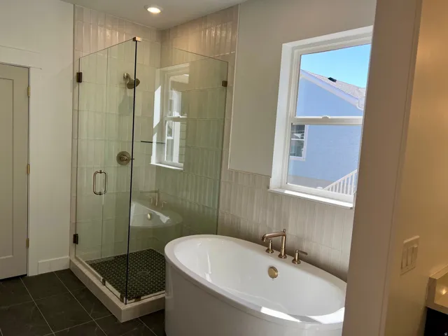 Contemporary bathroom featuring a freestanding soaking tub with bronze-finish fixtures, a glass-enclosed shower with a dark tiled floor, and vertical subway tile accents