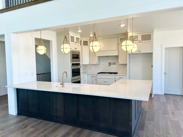 Open-concept kitchen featuring an oversized island with white countertop, recessed sink, and brass faucet