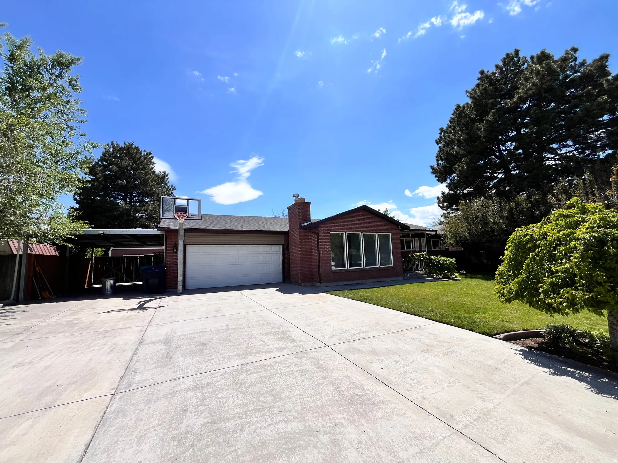 Brick exterior with a large front lawn, a wide concrete driveway, a two-car garage, and an attached carport