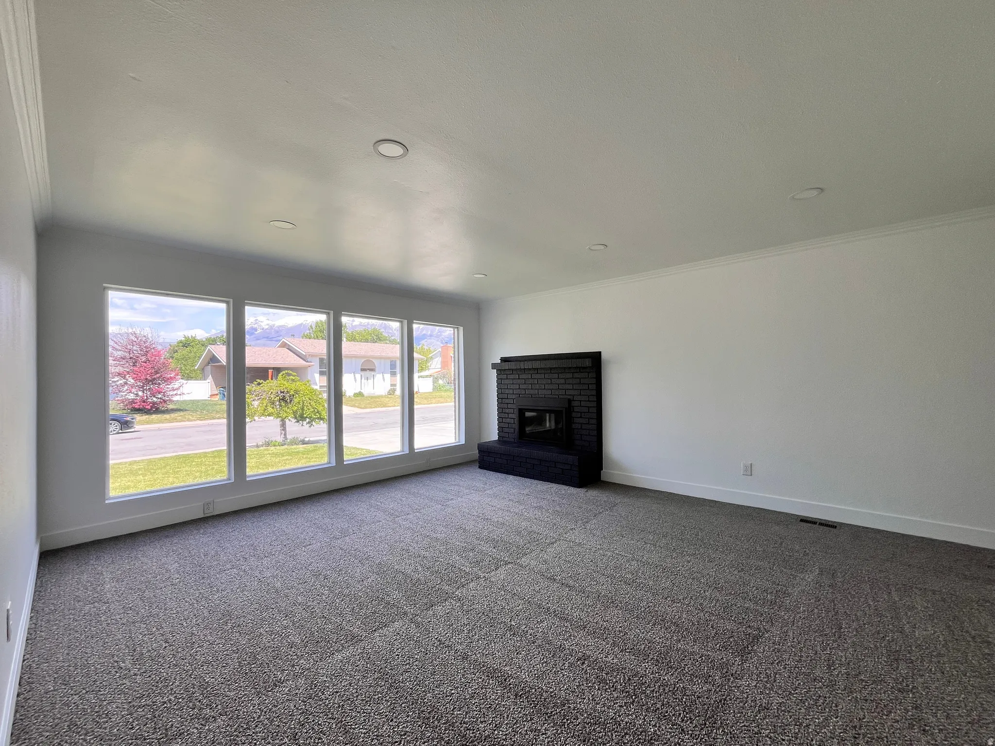 Living space featuring a black brick fireplace with a hearth, gray patterned carpet, recessed lighting, and crown molding