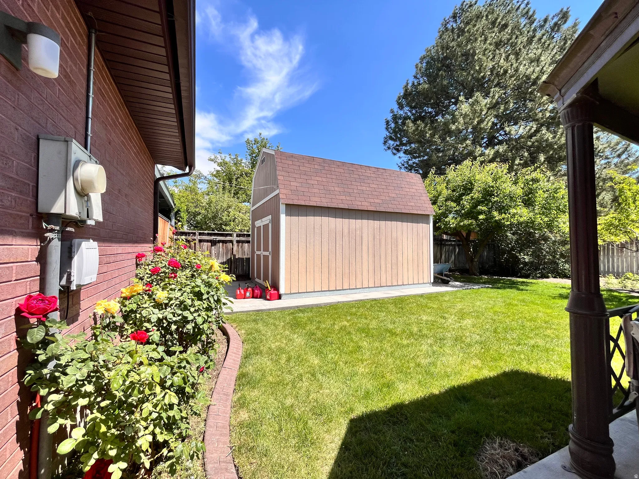 Expansive backyard featuring a storage shed with a shingle roof, a red brick exterior, a paved patio, and mature landscaping