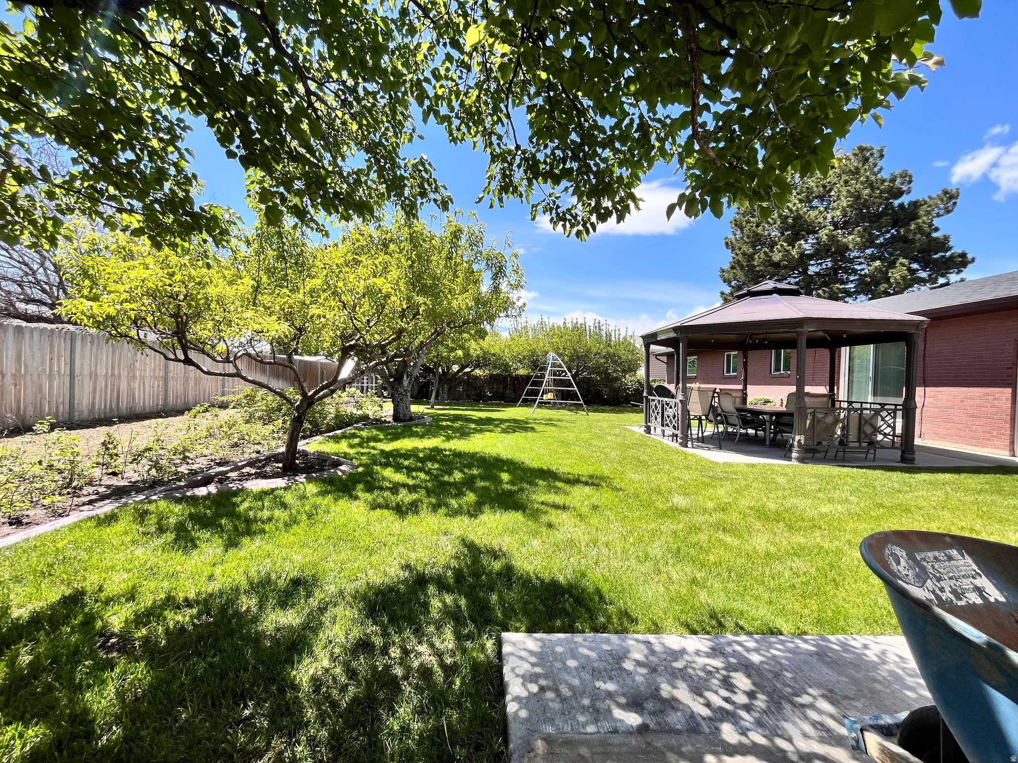 Expansive green lawn featuring mature trees, a private wooden fence, and a covered patio structure with a hardtop gazebo