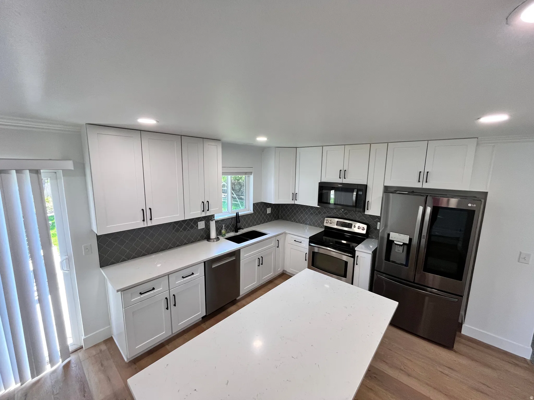 Kitchen featuring white shaker cabinetry with dark hardware, a dark gray diamond-patterned backsplash, white countertops, and stainless steel appliances