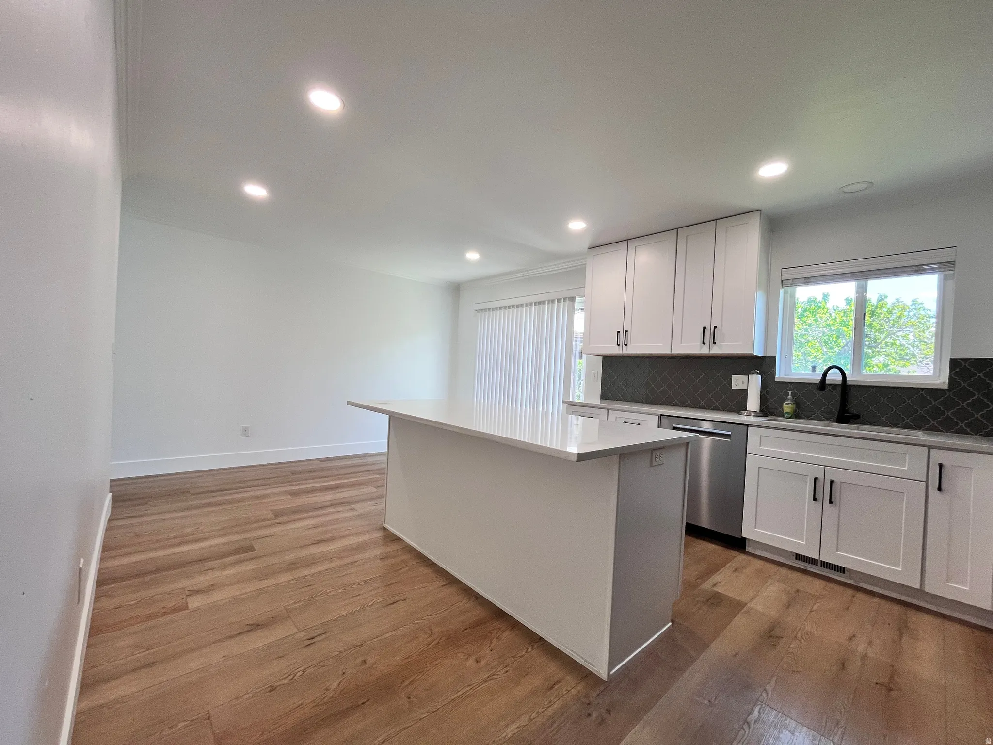 Open-concept kitchen featuring a large central island with white countertop, white shaker cabinetry, stainless steel appliances, and wood-finish flooring