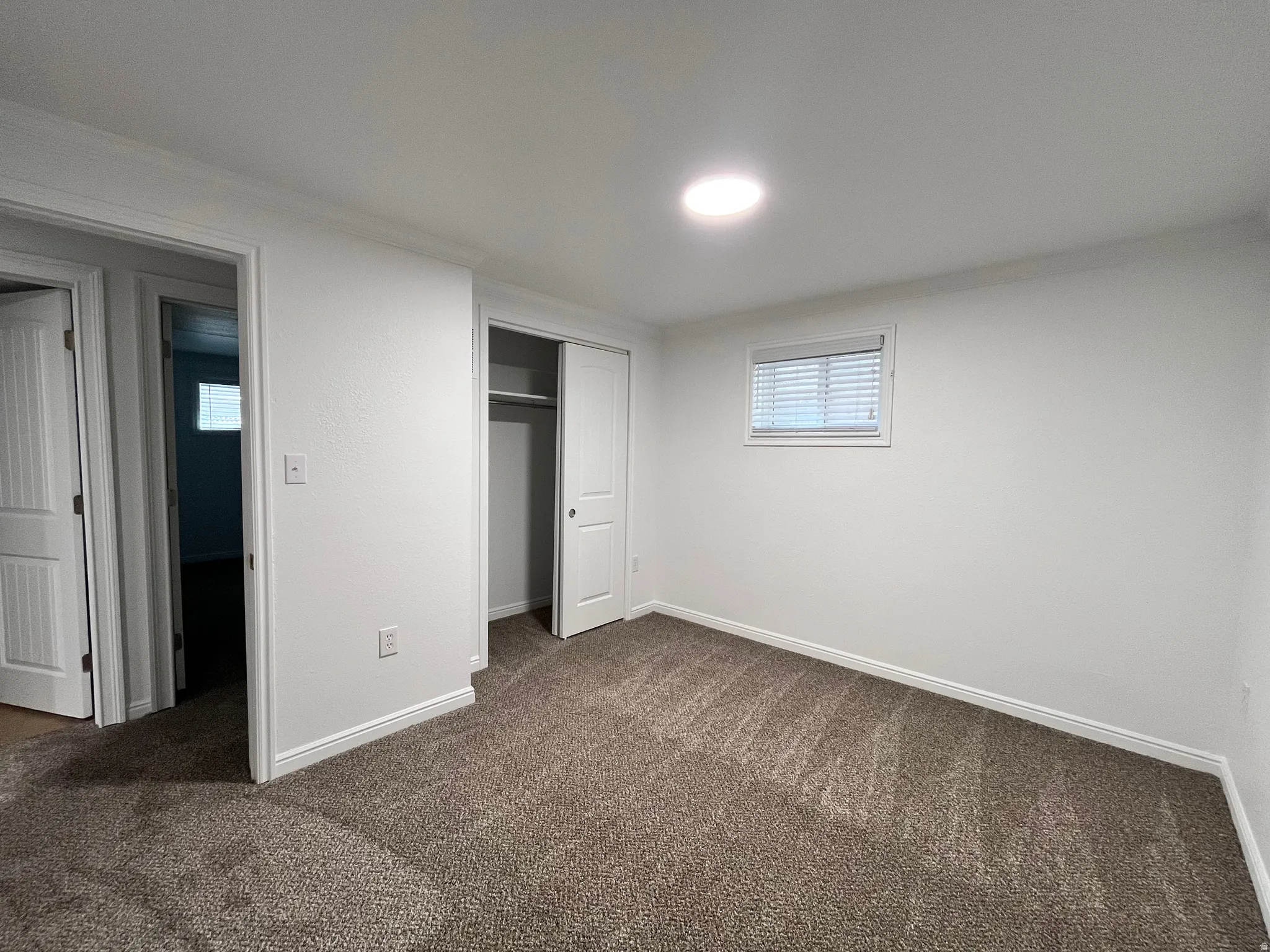 Carpeted room featuring white walls, a recessed light fixture, a window with blinds, and a closet with bifold doors
